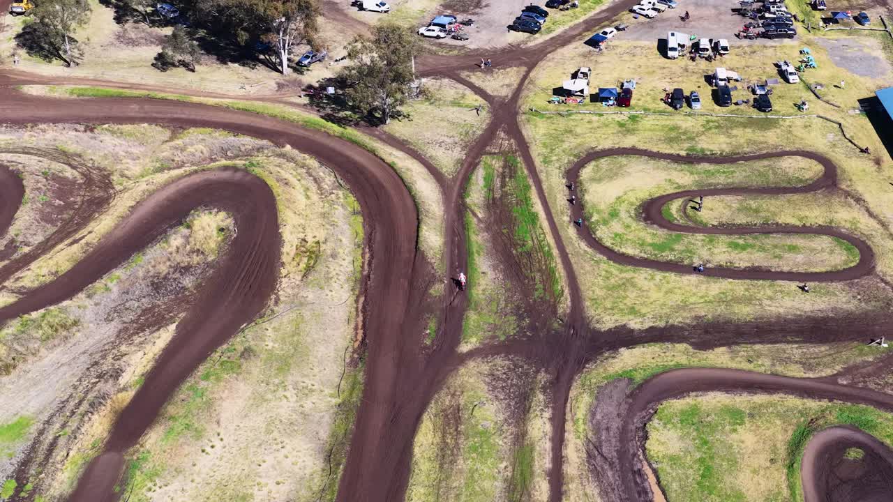 Drone captures motorbikes racing on winding dirt track under bright daylight at rural motocross park