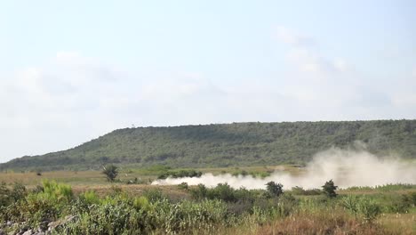 Military-vehicle-moving-though-training-ground,-wide-view