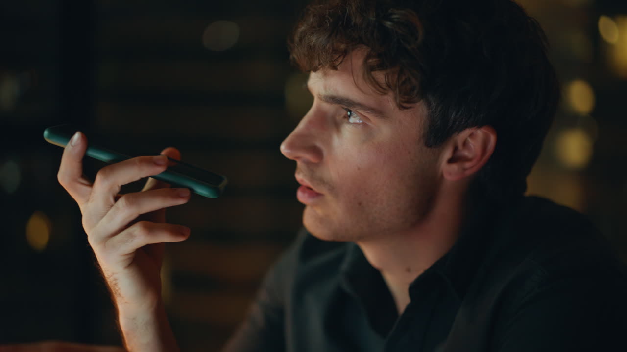 Serious employee talking loudspeaker cellphone at night office closeup