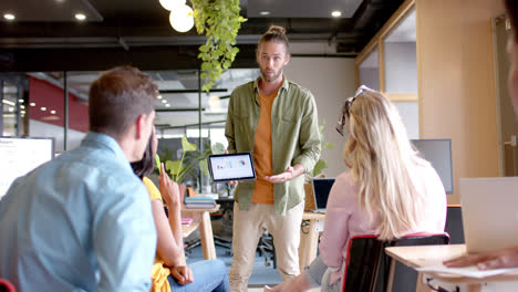 caucasian casual businessman presenting to diverse colleagues with tablet in office, slow motion