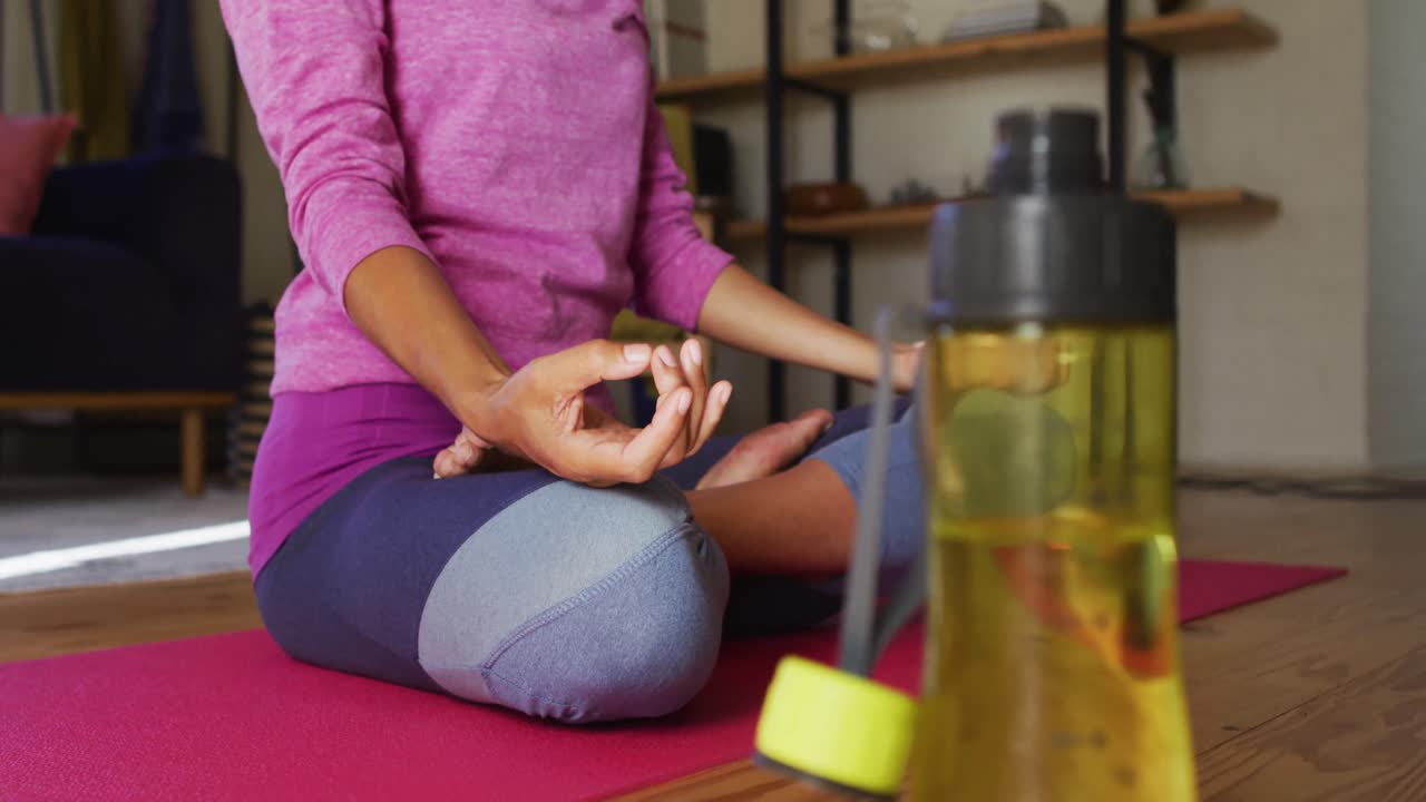 mujer de raza mixta practicando yoga y meditando mientras está sentada en un tapete de yoga en casa