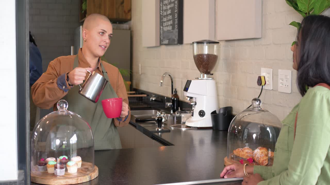 Barista entregando una taza roja a un cliente indio en el mostrador de la cafetería, vertiendo leche para servir café.
