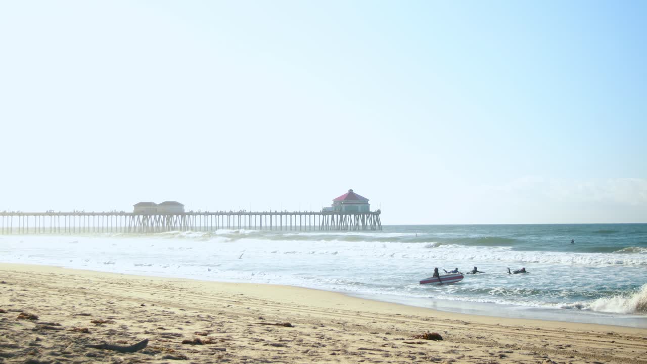 Una famiglia fa surf in spiaggia durante un'alba fosca con il molo di Huntington Beach sullo sfondo a Surf City USA California