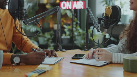 podcast co-hosts having discussion at desk with mics and planners in studio