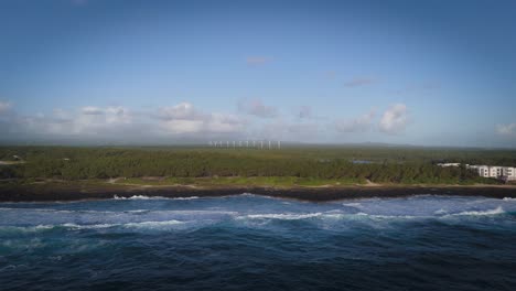 aerial view of powerful waves meeting the rocky mauritius coast with distant wind turbines on the horizon, symbolizing natural energy, sustainability, and coastal wilderness.