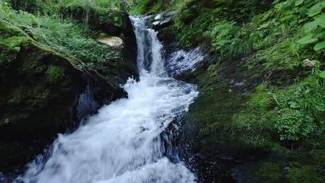aerial drone shot, approach to a small waterfall in a mountain forest adorned with lush vegetation