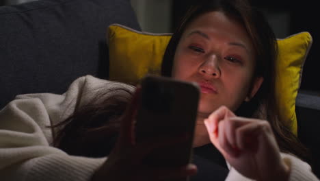 close up of woman spending evening at home lying on sofa with mobile phone scrolling through internet or social media 5