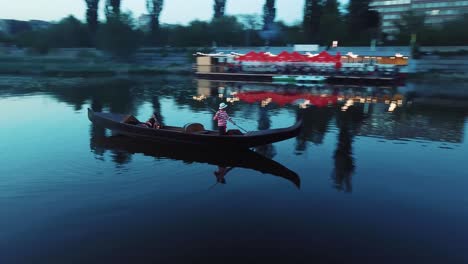 young woman floating in a boat and holding lantern at night. traditional venetian rowing boat with the gondolier and a female in the evening river. camera moves around.