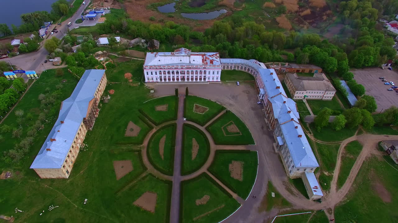 Round flower bed in the centre of architectural ensemble of old palace. Drone footage rising above the city scenery near the river.