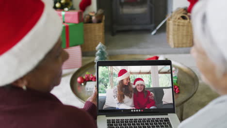 diversas amigas mayores que usan una computadora portátil para una videollamada de navidad con una familia feliz en la pantalla