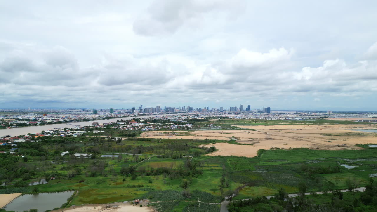 Aerial video of Phnom Penh looks across sand fields and green patches toward the downtown skyline