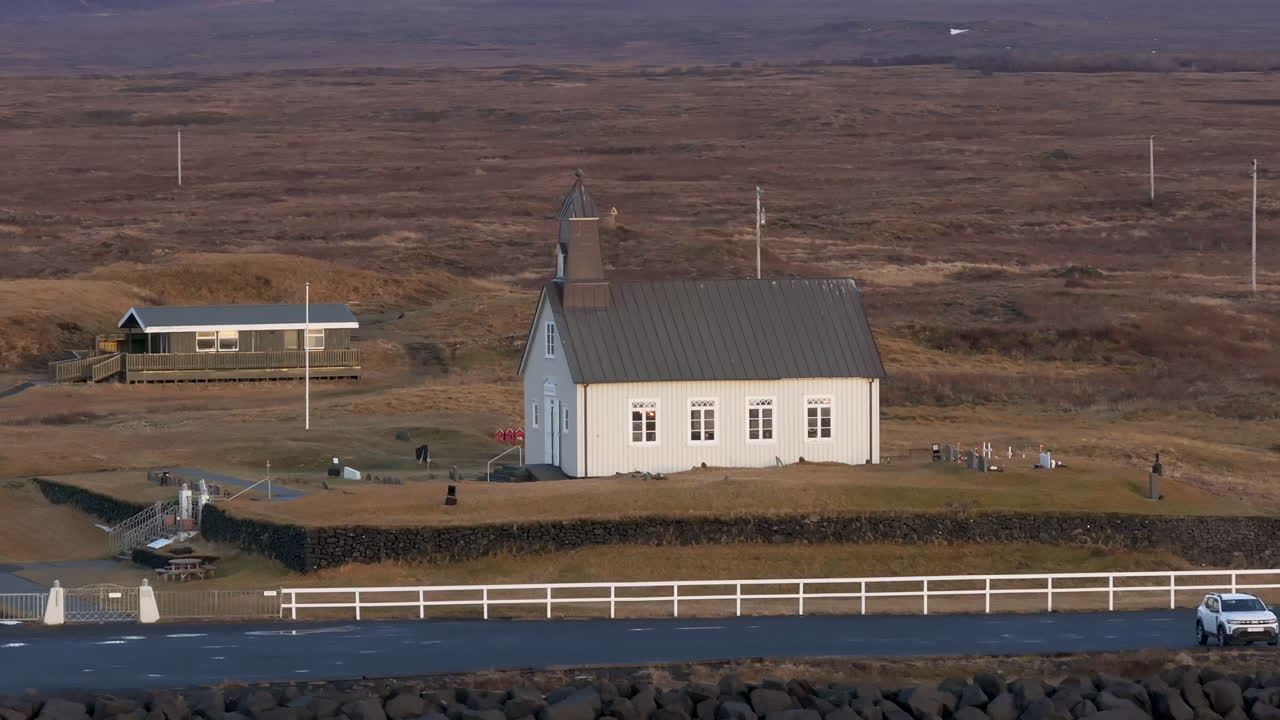 Luftfoto av Strandarkirkja kirke på Island, en historisk hvit kirke som står alene i et åpent landlig landskap omgitt av jorder og natur