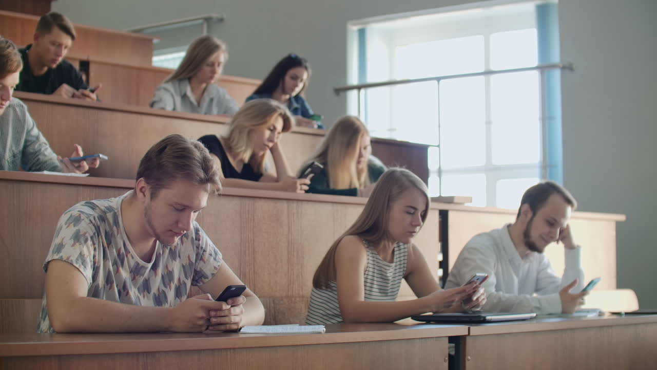 los estudiantes en una gran audiencia miran las pantallas de los teléfonos inteligentes y no se comunican en la vida real escriben mensajes sólo en línea