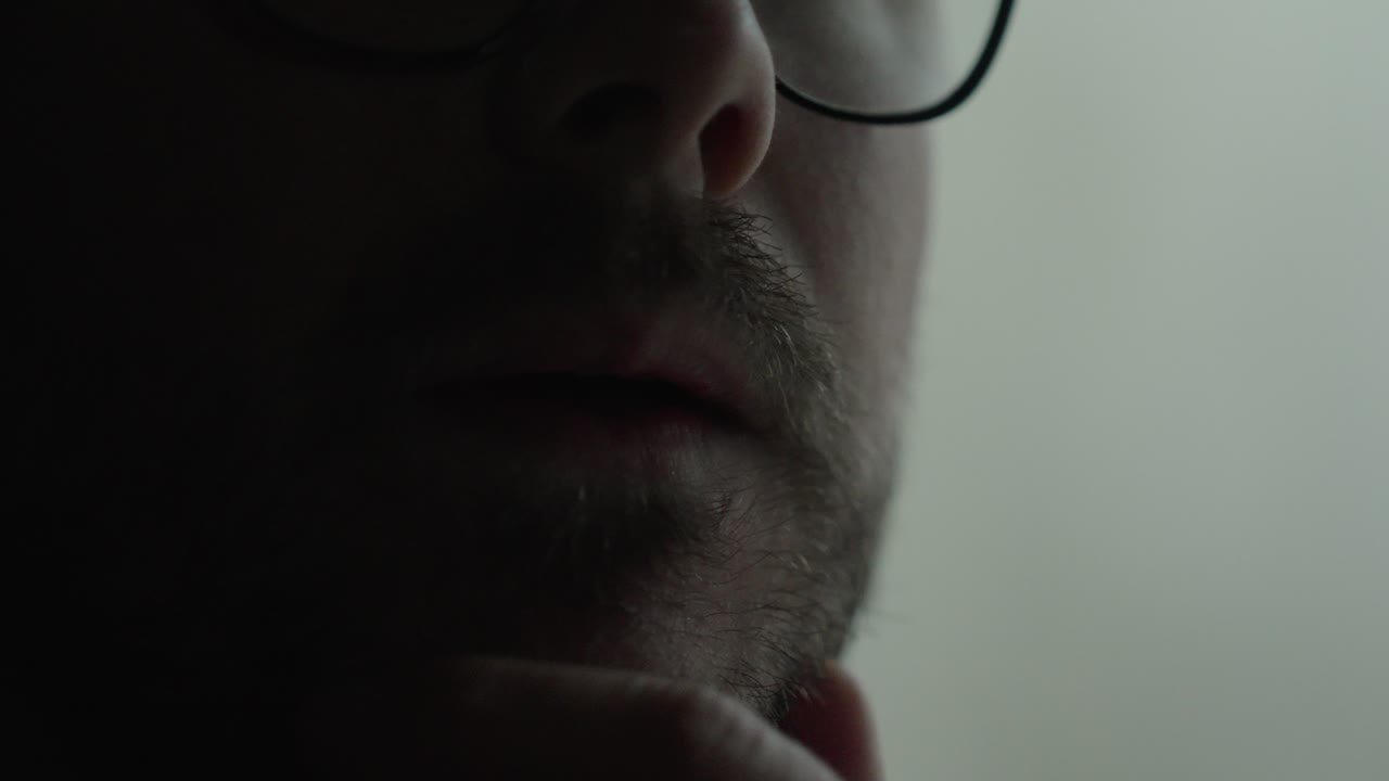 Moody close-up of a man near a window biting his finger in anxiety, suggesting suspicion, desperation, or inner conflict in low light. Ideal for concepts like stress, paranoia, guilt, fear, and psycho