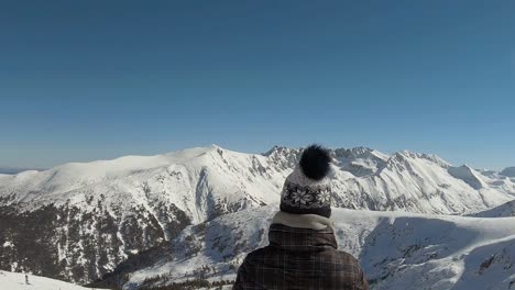 girl with winter hat at a top of a ski slope, looking at a horizon of mountains covered with snow