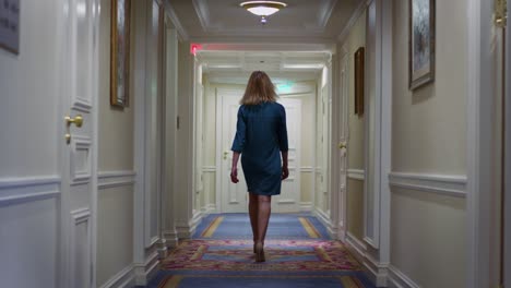 Young-woman-in-blue-dress-walking-along-hallway-corridor-at-cozy-hotel