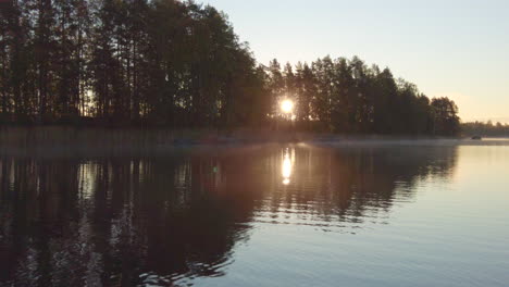 rising sun flares behind trees on a beautiful misty morning in calm lake scenery