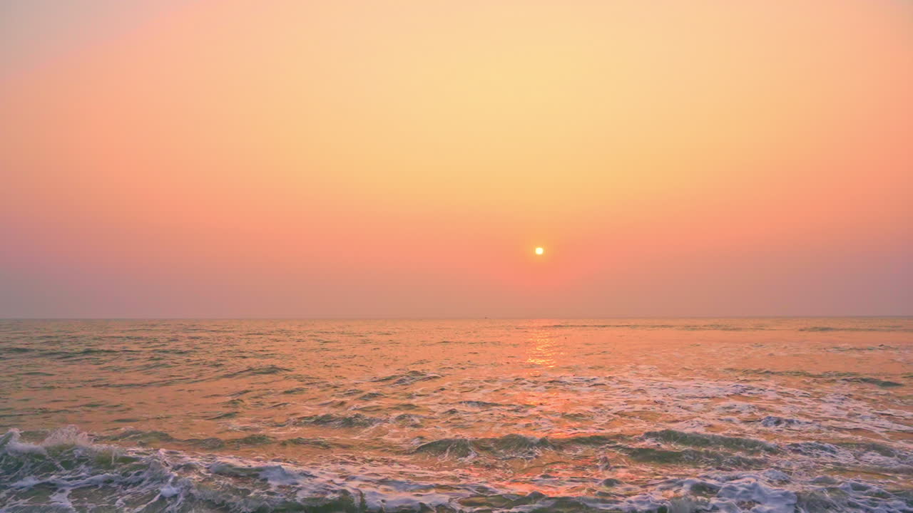 Beautiful golden hazy sunset over tropical ocean waves, wide shot
