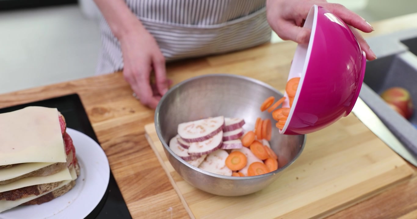 Female chef adds sliced carrots to cut eggplant on table