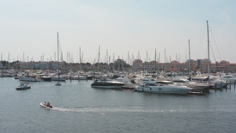 Cinematic-drone---aerial-shot-of-three-boats-on-a-marina-in-the-background-with-sailing-boats-on-a-sunny-day,-30p