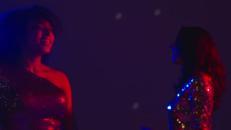 close up of two women in nightclub bar or disco dancing with reflected sparkling lights