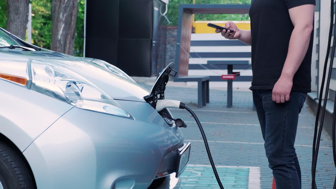 전기 자동차의 연료 충전 과정: 전기 에코 자동차가 충전하는 치 아래의. 전기 자동차 충전 치는 자동으로 열립니다. 남성 손이 발기 된 자동차를 입합니다.