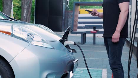proceso de reabastecimiento de combustible de un automóvil eléctrico. un disparo debajo de la escotilla donde se carga el automóvil ecológico eléctrico. la escotella de carga del automóvil eléctrico se abre automáticamente. una mano masculina inserta un automóvil erecto