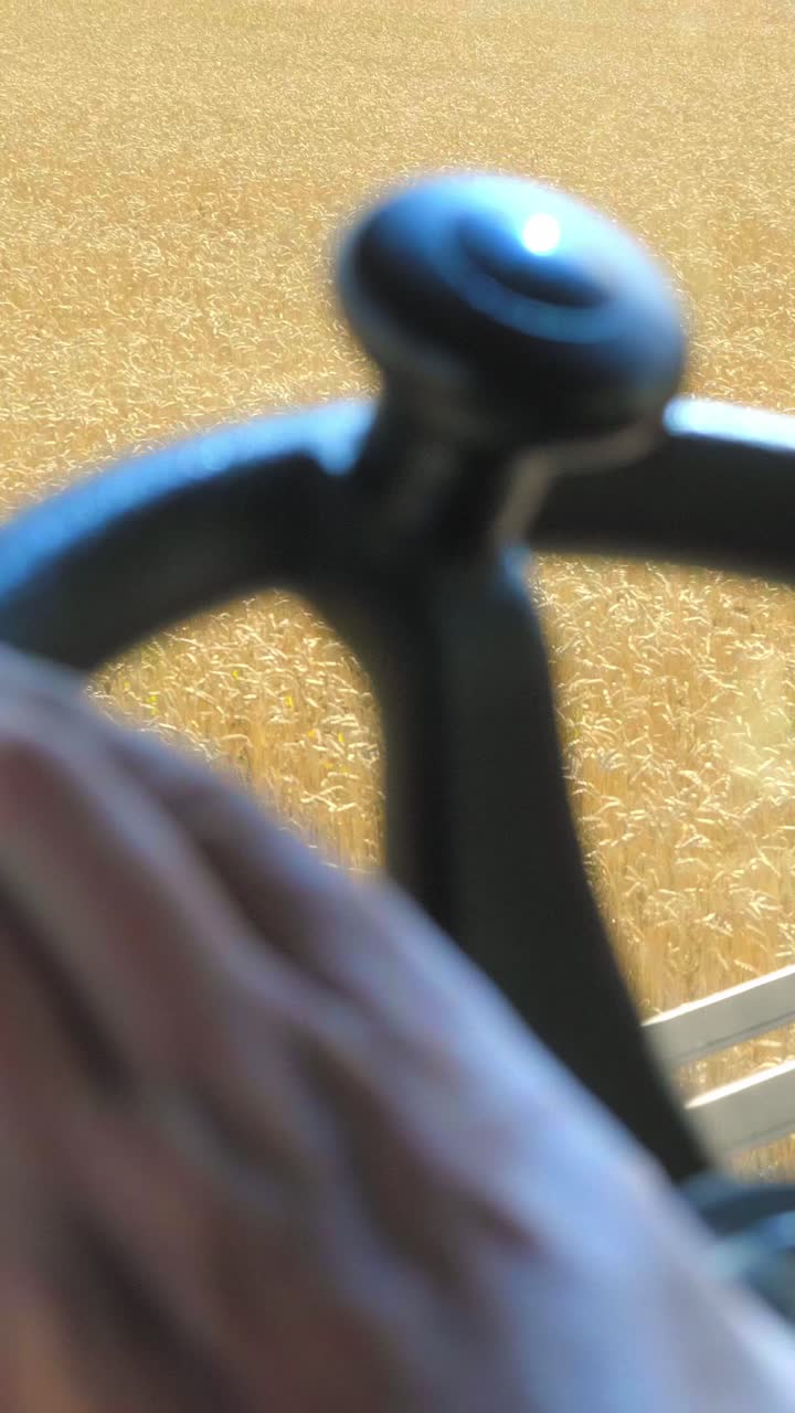 Close-up of farmer's hand on steering wheel of agricultural machinery in golden wheat field