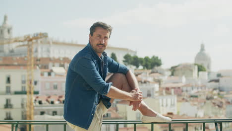 vista frontal del hombre de pie y mirando hermosas vistas de la ciudad, y luego, mira a la cámara