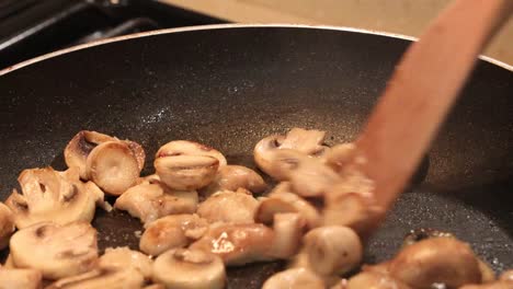 Primer-Plano-De-Champiñones-En-Rodajas-Salteados-En-Mantequilla,-Revueltos-Con-Una-Cuchara-De-Madera