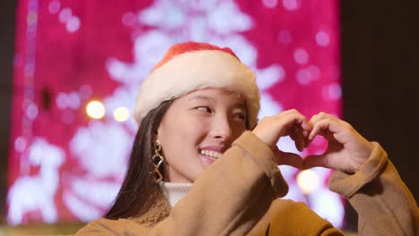 Festive woman wearing a Christmas hat making a heart shape