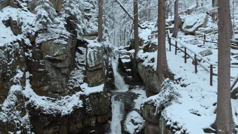 aerial view of a waterfall, in middle of cliffs and forest, in the karkonosze mountains, on a overcast, winter day, in poland - pull back, drone shot