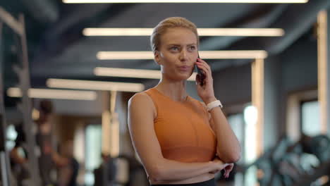 Smiling-athlete-woman-using-cellphone-in-sport-club.-Sporty-girl-standing-at-gym