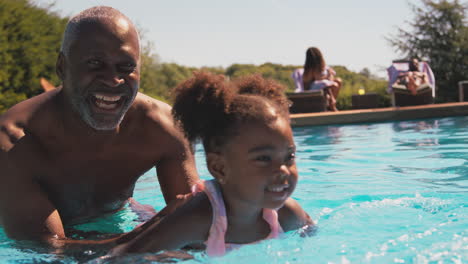 Abuelo-Enseñando-A-Su-Nieta-A-Nadar-En-La-Piscina-Al-Aire-Libre-Durante-Las-Vacaciones