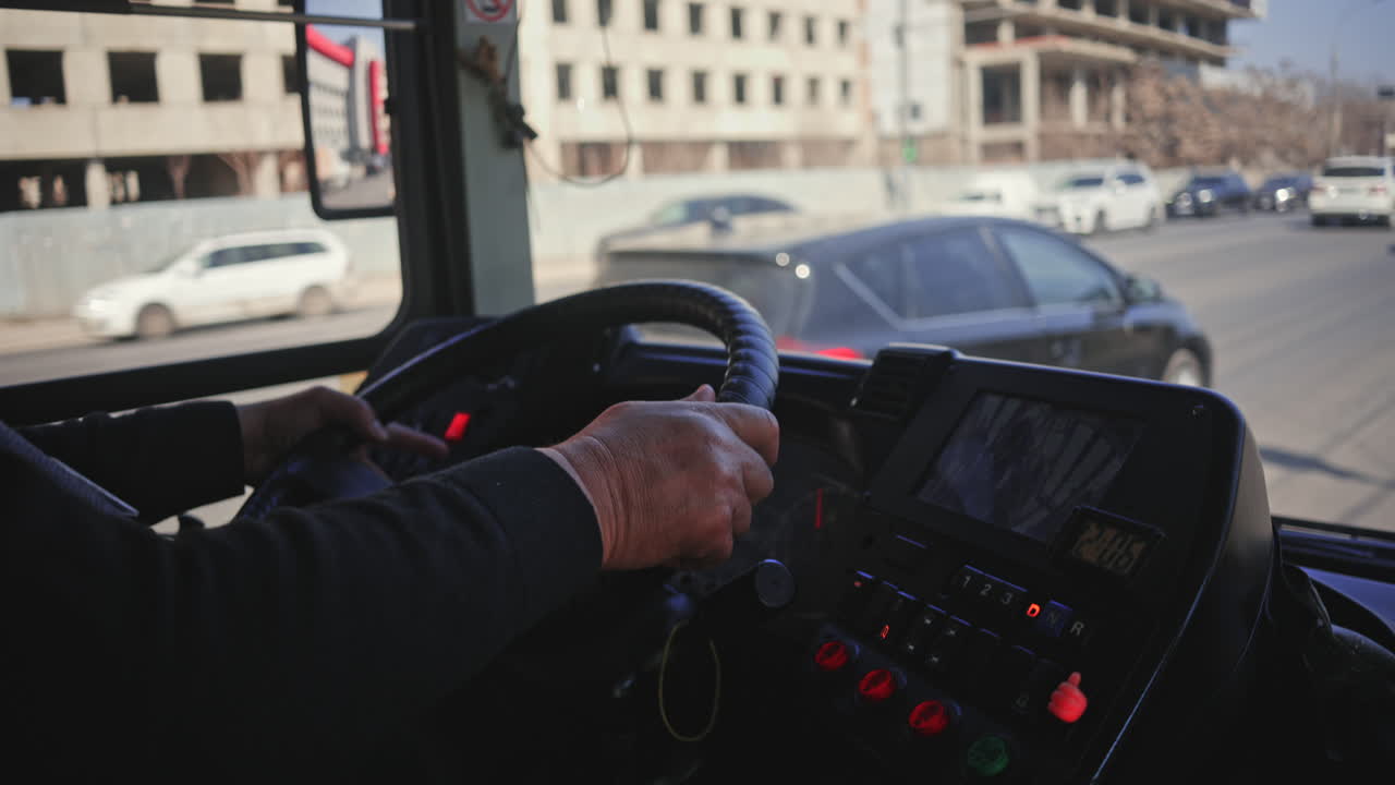 Vista desde el interior de un autobús, mostrando las manos del conductor en el volante y el tráfico por delante