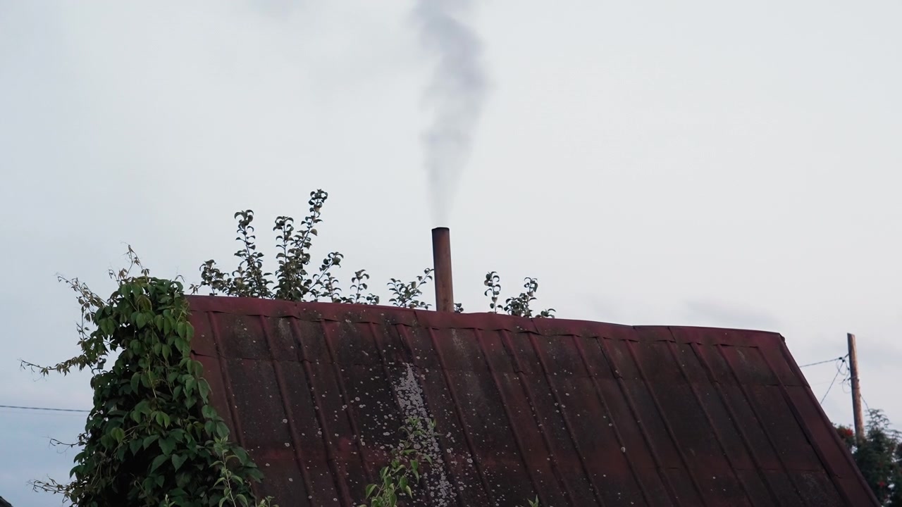 Smoke Rises from a Chimney on a Red Roof Against a Cloudy Sky