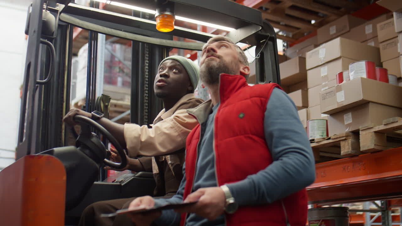 Two male workers inspecting inventory in a warehouse with a forklift