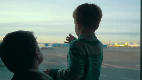 hijo y padre mirando el área del aeropuerto a través de la ventana
