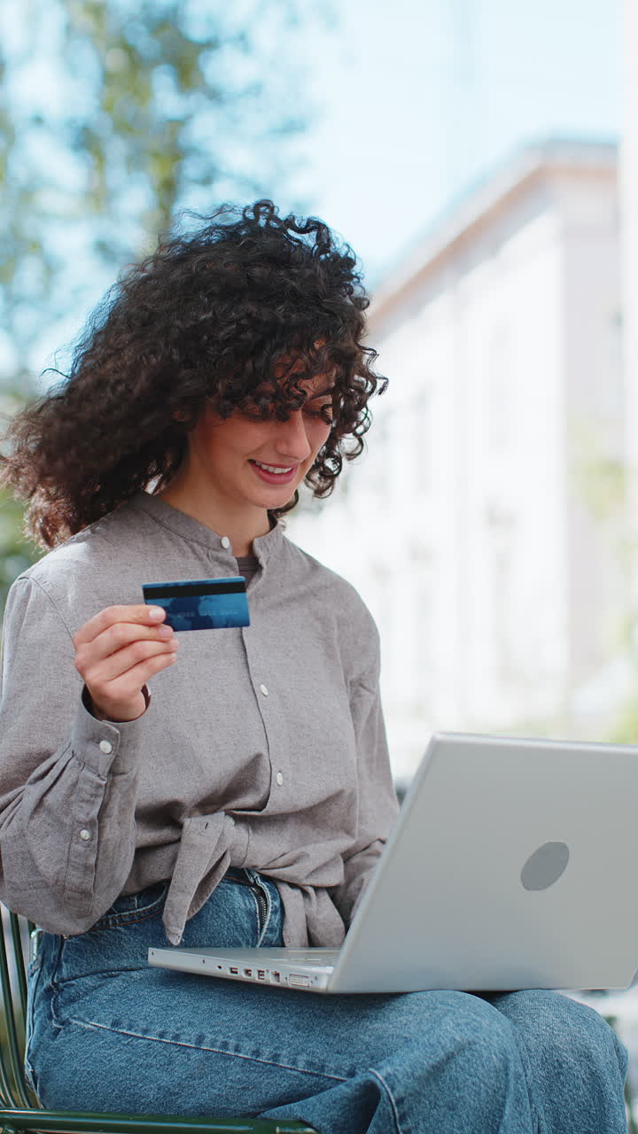 Giovane donna caucasica che utilizza una carta di credito e un portatile per trasferire denaro e fare acquisti online