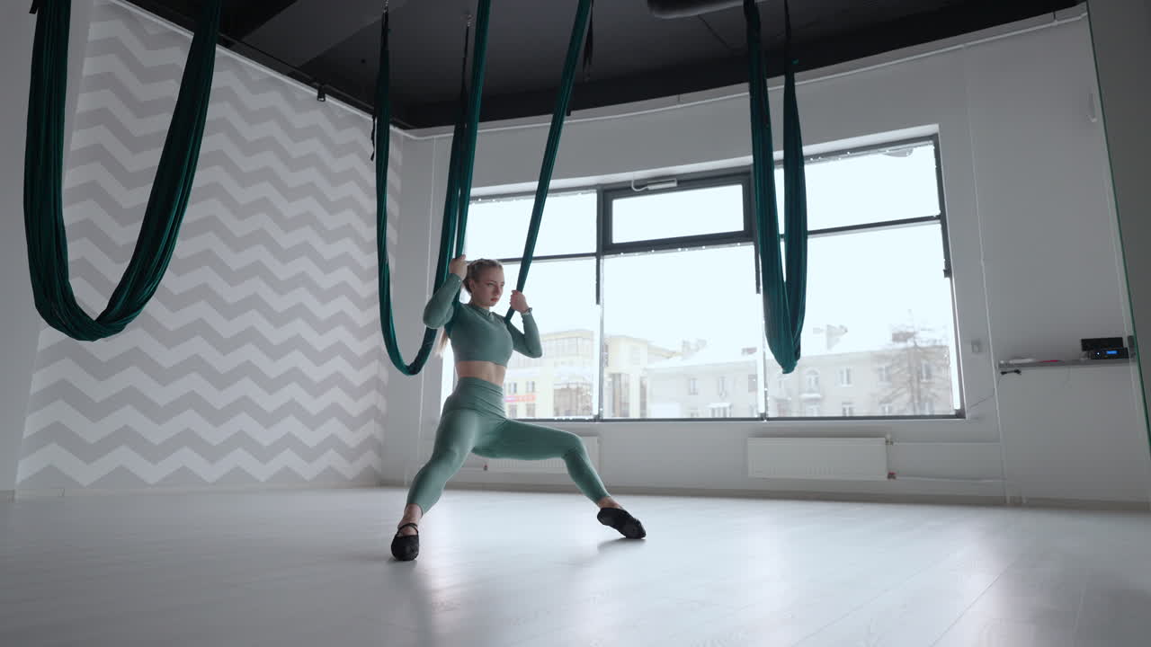 entrenador de fitness atractivo haciendo ejercicios de yoga de vuelo aéreo antigravedad en hamaca verde. mujer joven flexible práctica en aero estiramiento swing en el club de fitness. concepto de rutina de yoga de fitness femenino