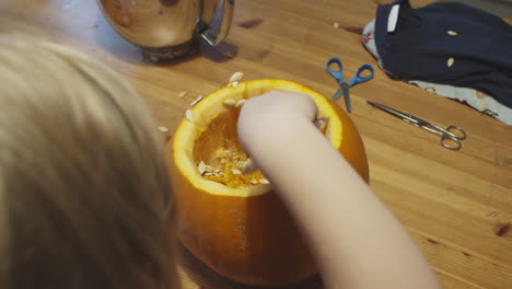 Little-girl-hollowing-out-a-pumpkin-with-a-spoon,-surprised-as-the-seeds-fly-out