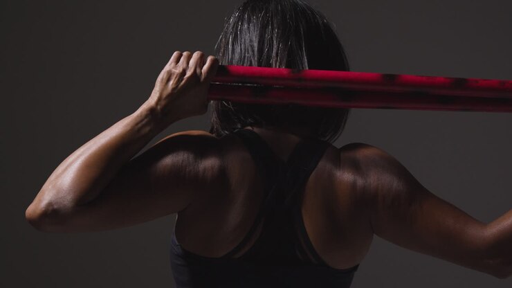 vista trasera de estudio de una mujer madura con ropa de gimnasia haciendo ejercicio con palos de artes marciales escrima 1