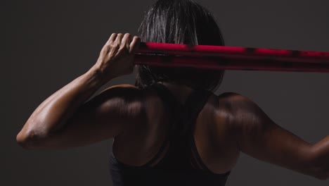 vista trasera de estudio de una mujer madura con ropa de gimnasia haciendo ejercicio con palos de artes marciales escrima 1