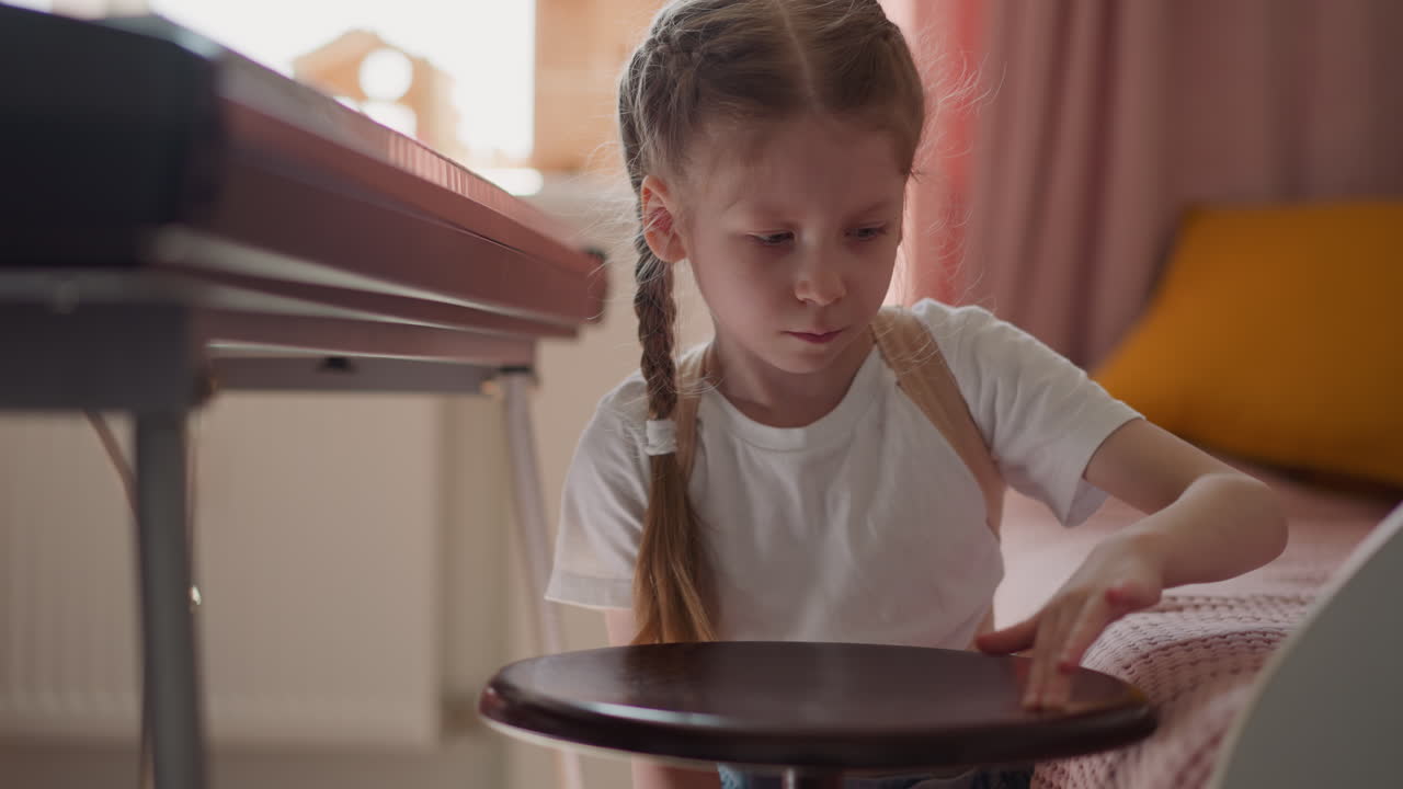 спокойная маленькая девочка поворачивает стул для фортепиано с помощью синтезатора.