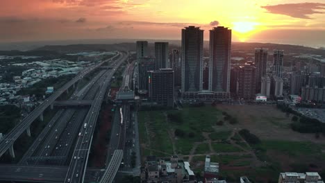 aerial flight over mrt station of linkou district in taipei city during golden hour. traffic on the highway against golden sunset. taiwan,south east asia.