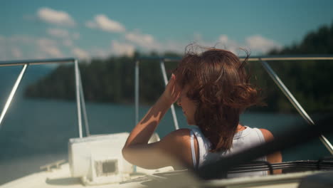 carefree woman with chestnut hair waved by wind rides modern yacht on sunny day. happy tourist enjoys sea cruise on summer vacation. boat sailing