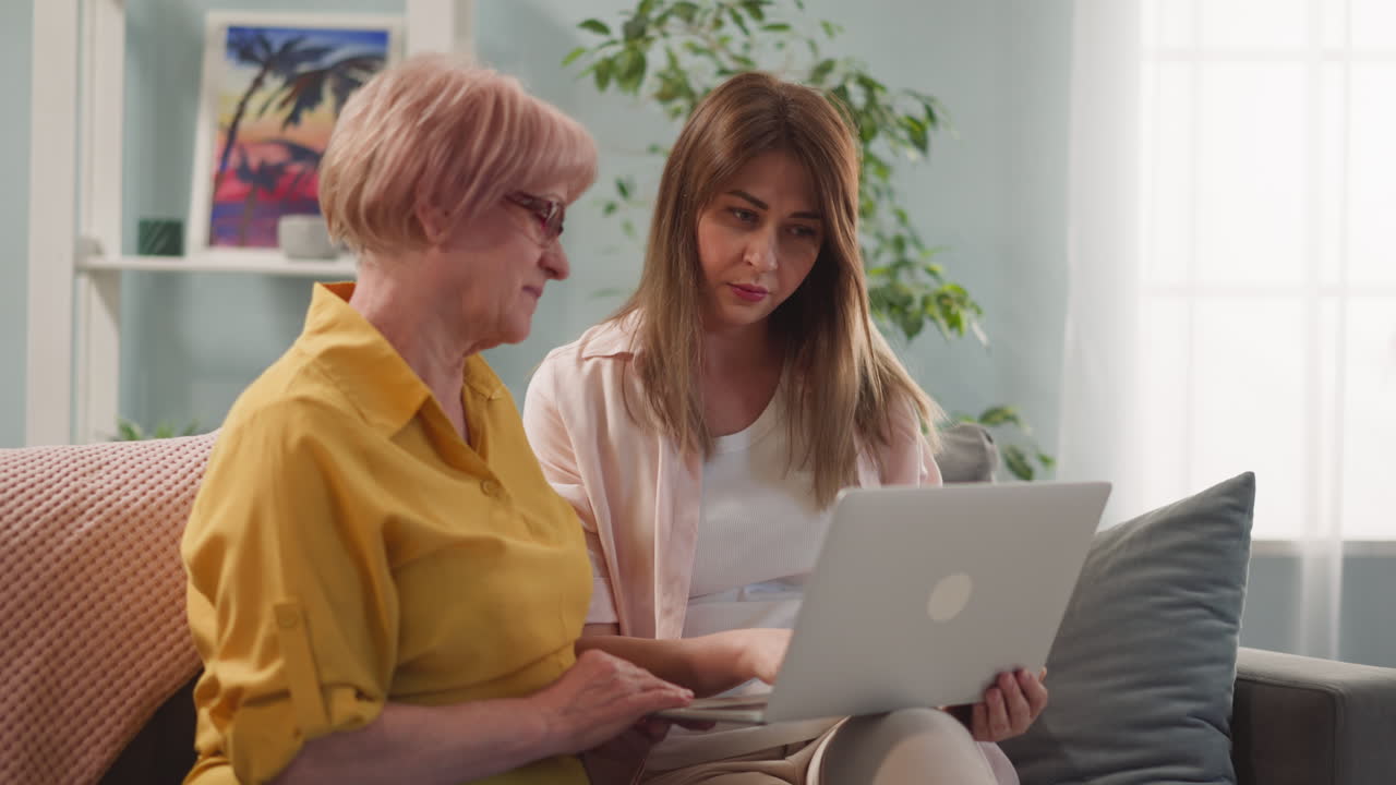 Daughter shows video on laptop to senior mother at home