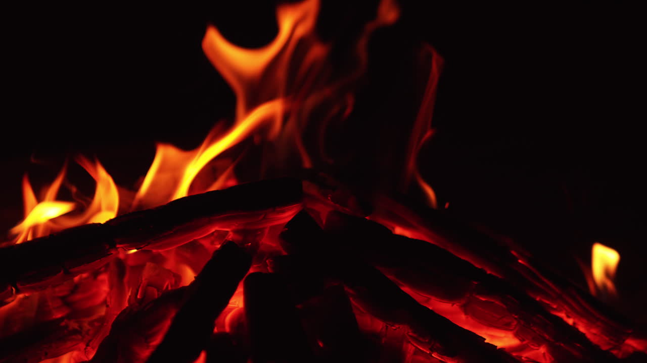 Smoldering embers of campfire close up. Little flame burning out in bonfire. Dark backdrop.