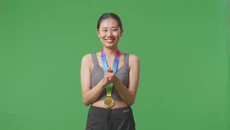 asian woman wearing a gold medal and clapping hands being proud winning as the first winner on green screen background in the studio