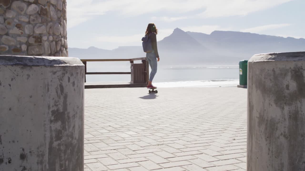 vista trasera de una mujer de raza mixta patinando en un soleado paseo marítimo junto al mar